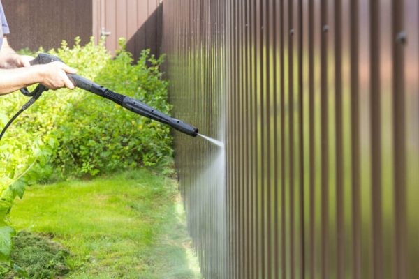 A man is using a hose to pressure clean a garden fence.